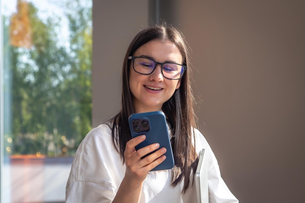 Веселая молодая женщина в очках со смартфоном в руках