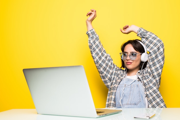 Cheerful young woman in headphones dancing to music while sitting in front of computer