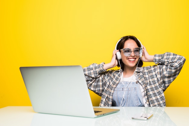 Cheerful young woman in headphones dancing to music while sitting in front of computer