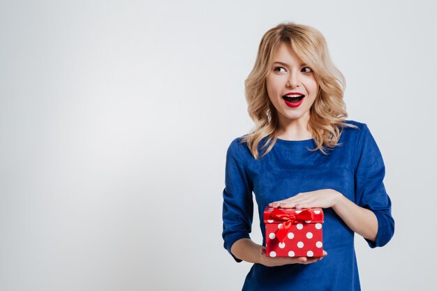 Cheerful young woman holding gift box over white wall