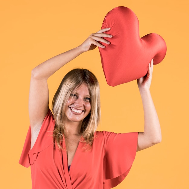 Cheerful young woman holding red heart cushion in hand