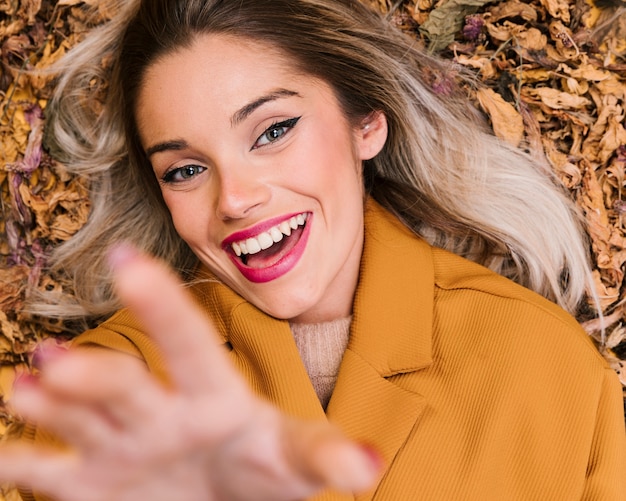 Cheerful young woman lying on dry leaves at outdoors