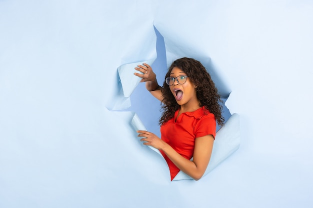 Free photo cheerful young woman poses in torn blue paper hole background, emotional and expressive