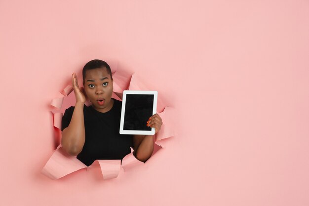 Cheerful young woman poses in torn coral paper hole