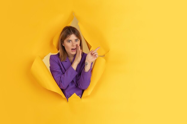 Cheerful young woman poses in torn yellow paper hole, emotional and expressive