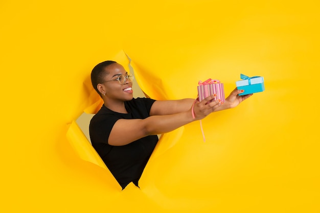 Cheerful young woman poses in torn yellow paper hole wall emotional and expressive