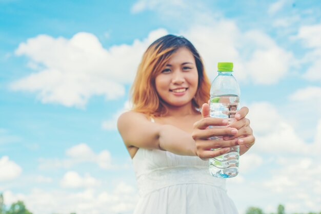 Веселая молодая женщина, показывая бутылку воды с зеленой крышкой
