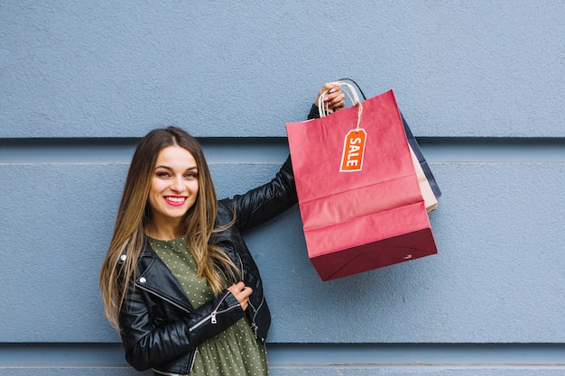 Free photo cheerful young woman standing in front of wall holding many colorful shopping bags