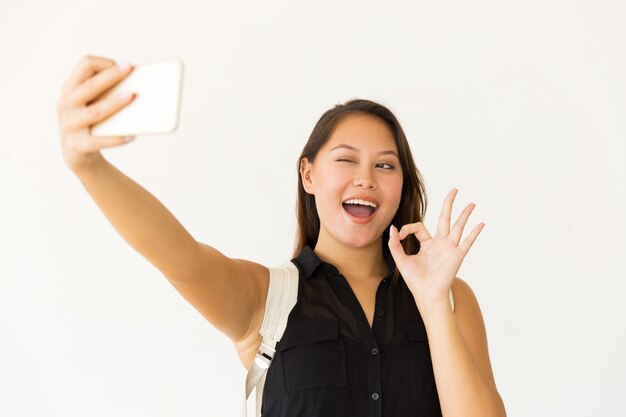 Cheerful young woman taking selfie with smartphone