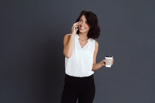 Веселая молодая женщина разговаривает по телефону и держит кофе в руке