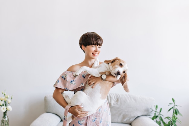 Cheerful young woman in trendy wristwatch holding her big puppy with black nose and laughing