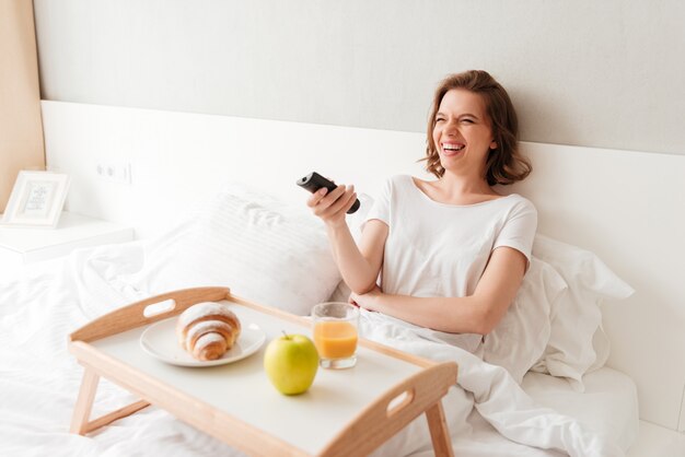 Cheerful young woman watch tv holding remote control.