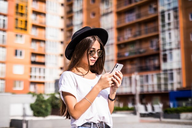 メッセージを入力する街で黒い帽子をかぶっている陽気な若い女性。