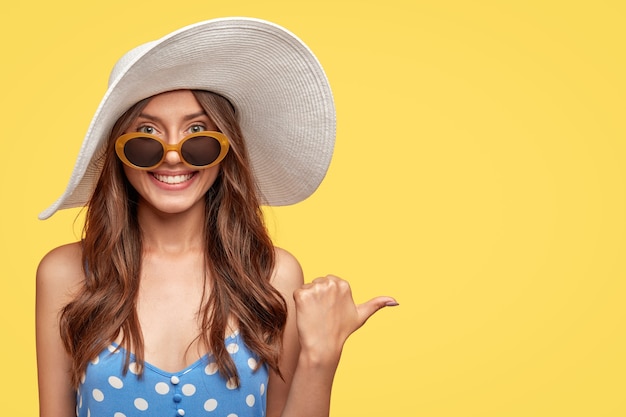 Foto gratuita allegro giovane donna che indossa un cappello in posa contro il muro giallo