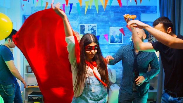 Cheerful young woman wearing a superhero red cape while partying with his friends. Neon lights.