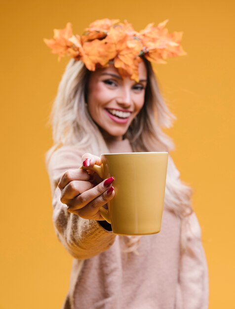 コーヒーカップを保持している葉の花輪を身に着けている陽気な若い女性