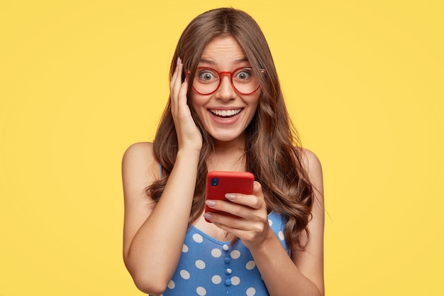 Cheerful young woman with glasses posing against the yellow wall