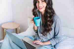 Free photo cheerful young woman with mug and laptop