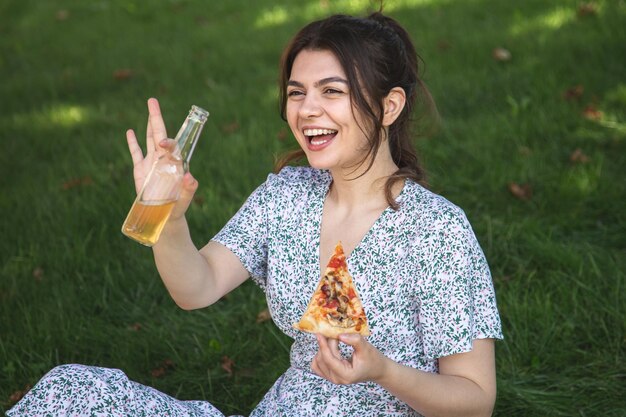 Foto gratuita giovane donna allegra con un pezzo di pizza ad un picnic