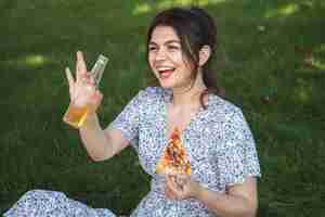 Free photo cheerful young woman with a piece of pizza at a picnic