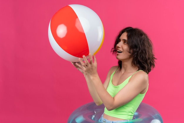 A cheerful young woman with short hair in green crop top smiling and holding inflatable ball