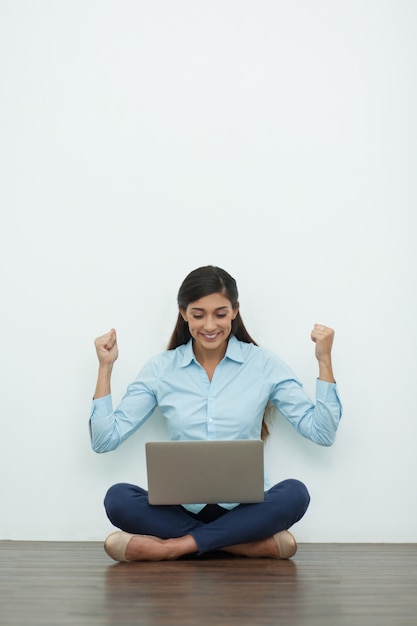 Free photo cheerful young woman working on laptop on floor