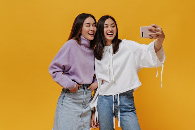 Cheerful young women in denim outfits smile on isolated