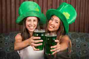 Free photo cheerful young women showing glasses of drink on settee