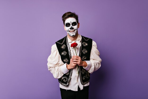 꽃과 함께 포즈를 취하는 흰 셔츠에 쾌활한 좀비 남자. 빨간 장미와 함께 blithesome 백인 남자의 실내 사진.