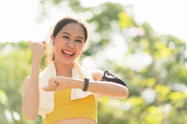 아침 달리기에서 환호하는 아시아 여성 스포츠 여성 운동선수는 조깅 달리기에 대해 예라고 말하면서 운동복을 입고 손목 시계에서 시간을 확인하는 승리를 기뻐합니다.