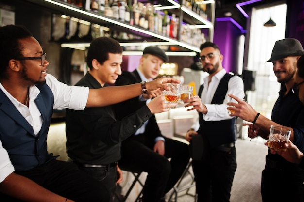 Cheers group of handsome retro welldressed man gangsters spend time at club drinking whiskey at bar counter multiethnic male bachelor mafia party in restaurant