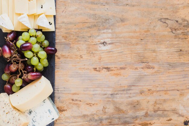 Cheese blocks and grapes on slate board over the wooden desk