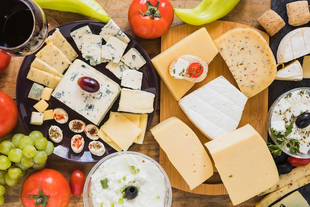 Cheese blocks and slices with tomatoes, grapes and green chili pepper on table