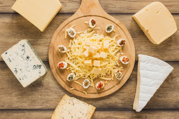 Cheese blocks surrounded near the wooden chopping board on wooden desk