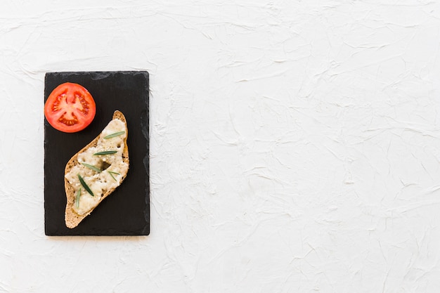 Сырный хлеб с томатным ломтиком на плите сланца над белым фоном