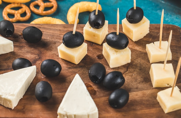 Cubi del formaggio ed olive nere su una tavola di legno con i cracker