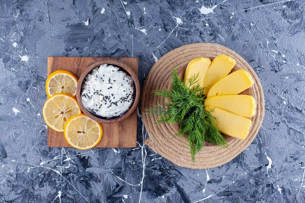 Cheese and dill in a bowl on a trivet next to a bowl of cheese and sliced lemon on a board , on the blue surface.