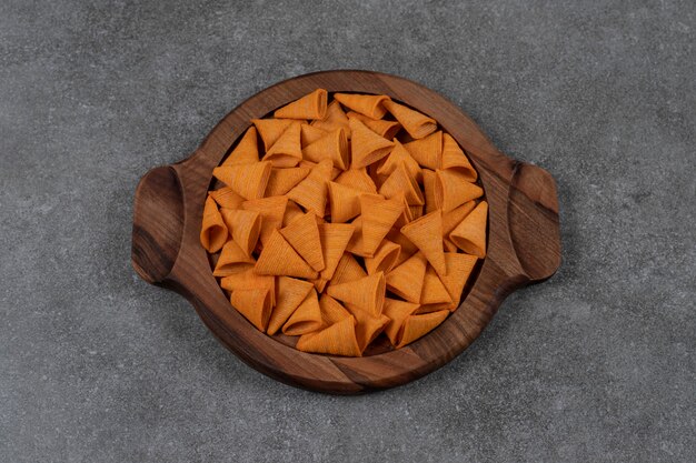 Cheese flavored cone shaped corn chips in wooden plate  on the marble surface