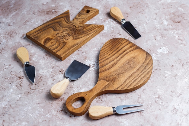 Cheese knives with wooden handles, fork, spatula on light brown surface.