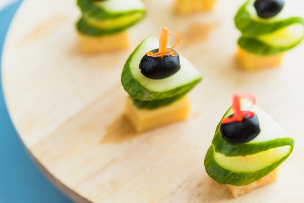 Cheese, olive and cucumber on plastic skewer on chopping board
