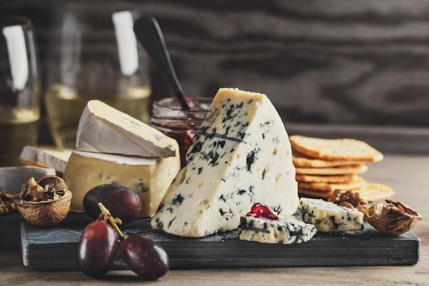 Cheese plate with different arts of cheese grape and nuts served on wooden board.