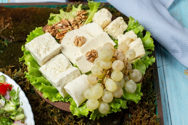 Сырная тарелка с белым сыром, зеленым виноградом и орехами.