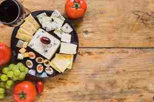 Foto gratuita vassoio di formaggi con pomodori e uva sulla scrivania in legno