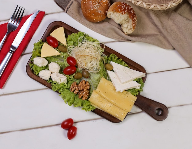 Бесплатное фото Сырная тарелка с помидорами, орехами и оливками со столовыми приборами и булочками вокруг.