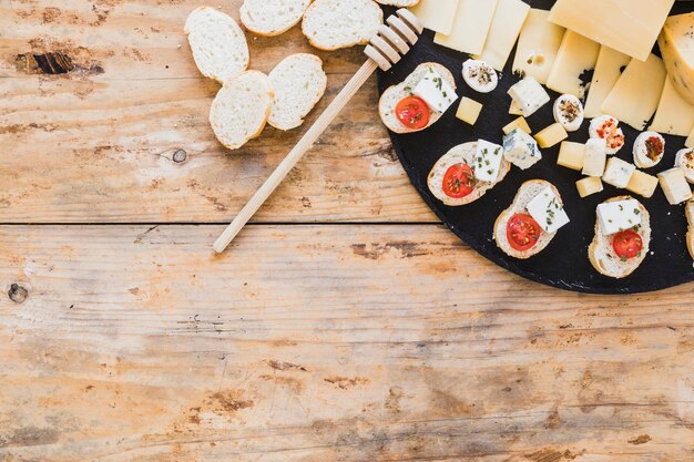 Cheese slices and bread appetizer with honey dipper on wooden desk