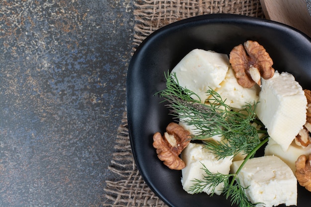 Бесплатное фото Ломтики сыра, укроп и ядра грецких орехов в черной миске.