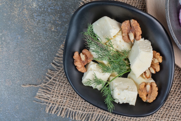 Ломтики сыра, укроп и ядра грецких орехов в черной миске.