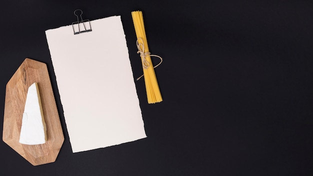 Cheese; spaghetti pasta and white blank paper on black backdrop