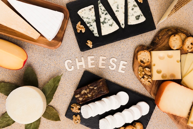 Cheese text surrounded with variety of cheeses slices; walnut and bay leaves over textured surface