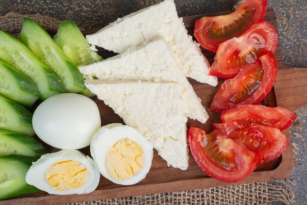 Cheese, tomatoes, boiled eggs and cucumbers on wooden board.